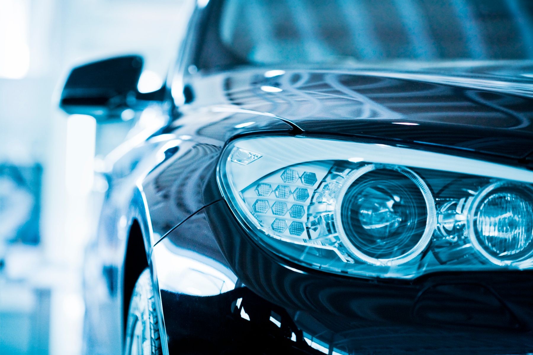 Close-up of a car's headlight and side mirror with a blue tint.